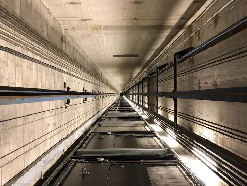 Подовжений вид усередині шахти ліфта, де видно паралельні рейки, кабелі та елементи конструкції, що простягаються вдалину.