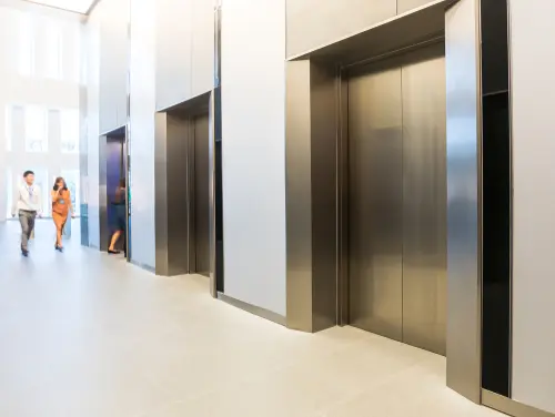 Лобі офісу з кількома дверима ліфта та двома людьми, що йдуть