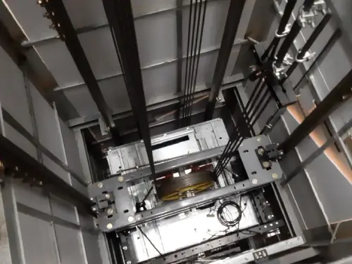 Внутрішній вигляд шахти ліфта, де видно механічні компоненти, кабелі та елементи конструкції.